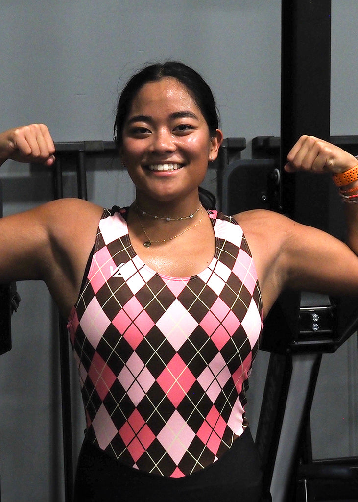Woman flexing in the gym wearing a JL Women's Totally Argyle Unisuit