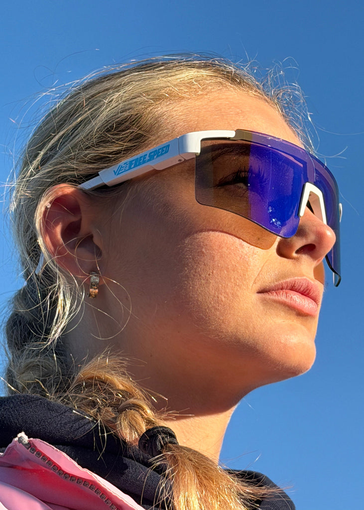 Person wearing blue and white sunglasses with a clear blue sky background